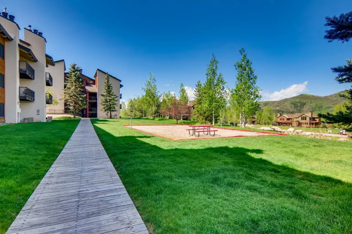 A wooden boardwalk meanders through lush greenery to a picnic area, with mountain views in the distance. The space is ideal for strolls, morning coffee, or outdoor games, and serves as a tranquil bridge between private condos and the shared amenities.