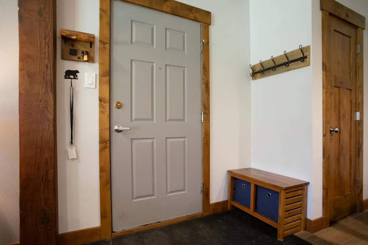 This image captures the home's entryway, featuring the front door, a wooden bench, and coat hooks. The space is organized for convenience, inviting guests to hang coats and store shoes as they enter, directly reflecting the ease of arrival described in the section.