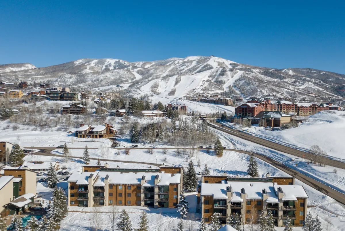 A scenic winter landscape showcasing snow-covered mountains, ski slopes, and nearby residential buildings nestled along the tree line. The image emphasizes proximity to world-class skiing and Steamboat's natural beauty, setting the stage for a winter adventure.