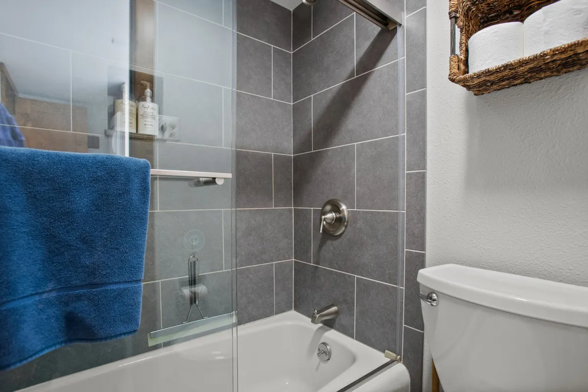 A calming bathroom featuring a glass shower enclosure, blue towel, and a basket with fresh towels. The atmosphere is spa-like, with an emphasis on relaxation and personal care routines, highlighted by designer tile and inviting decor.