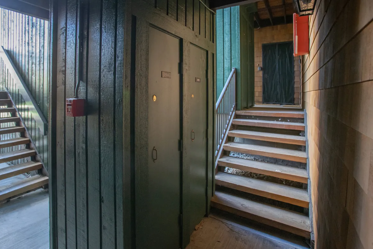 A functional view of a short staircase and hallway with green doors, signaling the minor 'step-down' from the parking lot to the unit, as well as easy navigation for guests and storage access.