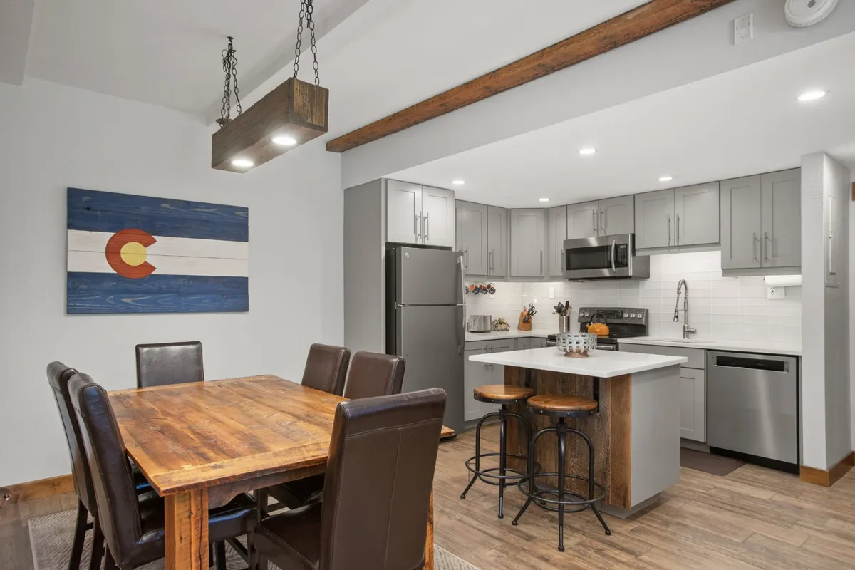 A spacious, open dining area featuring a sizable dining table set beside colorful wall art. The kitchen island is visible in the background, tying together the spaces for cooking, eating, and gathering. The scene evokes a sense of togetherness and is styled for both everyday meals and festive gatherings.