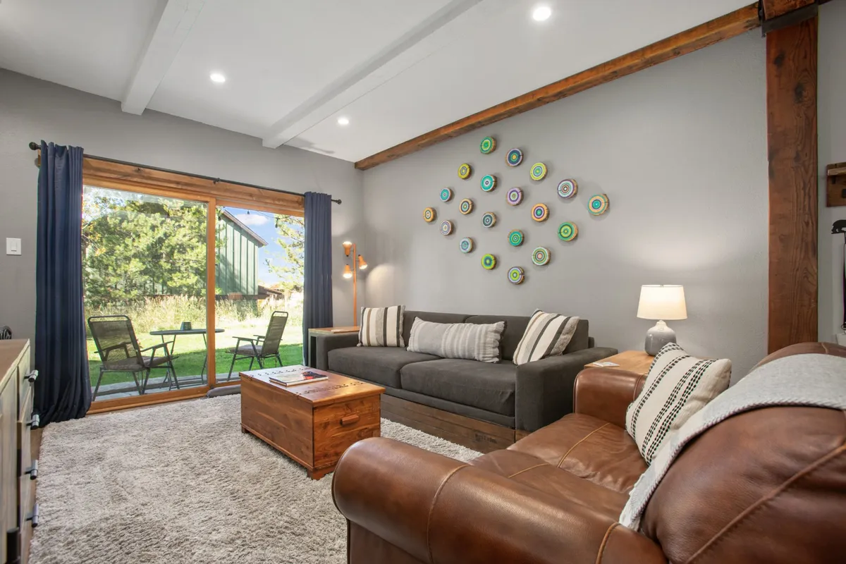 A comfortable seating area with a plush sofa and coffee table facing a sliding glass door. Decorative wall art adds personality, while sunlight pours into the room, creating a bright, relaxing space that feels connected to the outdoors.