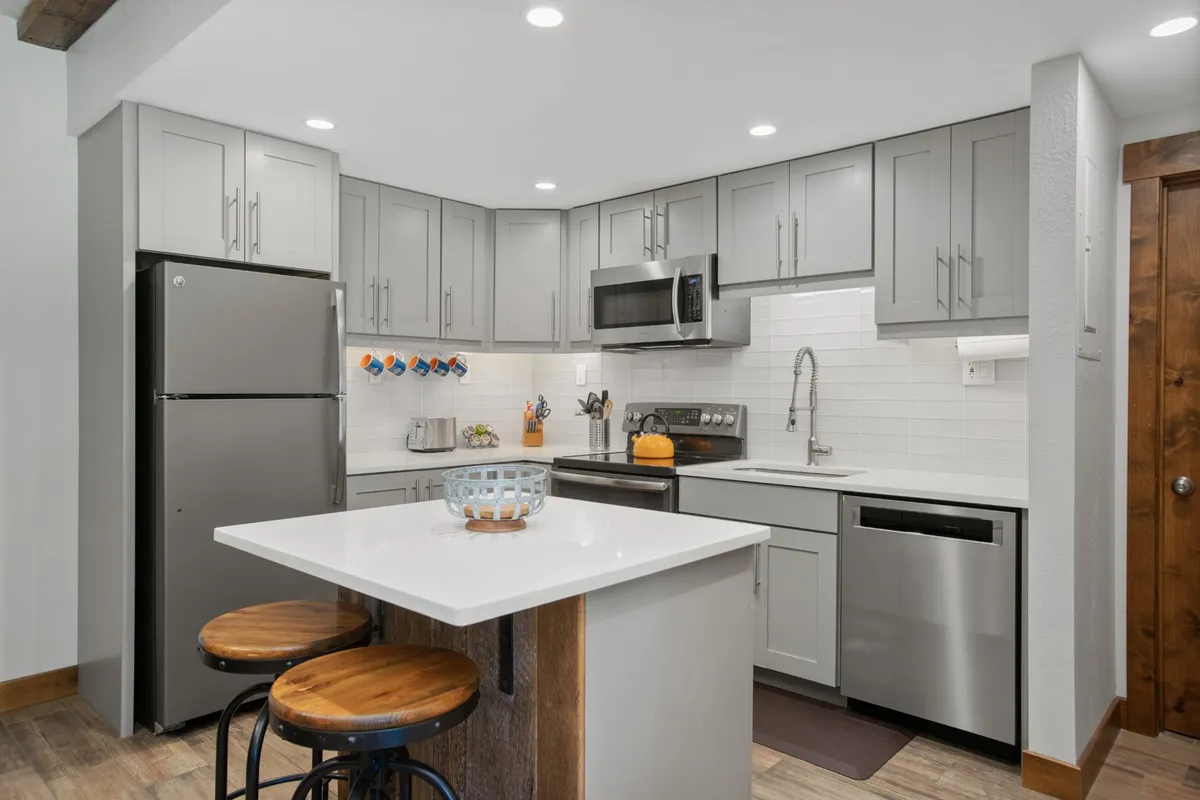 A modern kitchen with a prominent island countertop, gleaming stainless steel appliances, and colorful mugs hanging on the wall. The space is bright and functional, ideal for both casual cooking and entertaining guests.