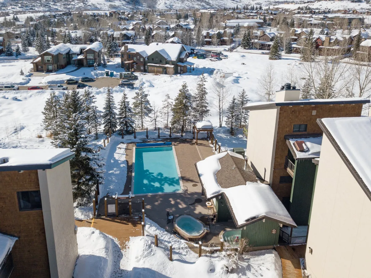A resort-style swimming pool and inviting hot tub framed by a snow-covered landscape, with a wooden deck and clear signs of winter. The scene evokes après-ski relaxation, featuring amenities available to guests after a day on the mountain.