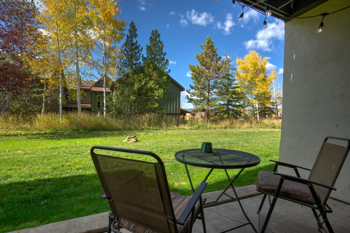 A tranquil exterior space with two comfortable chairs and a small table set on lush green grass, framed by colorful trees. The area feels private yet inviting, ideal for morning coffee, reading, or a small picnic, and it connects the home to the outdoors.