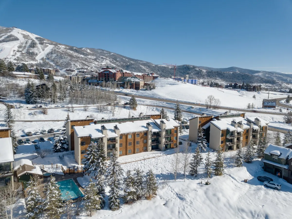 A bird’s-eye view of snow-dusted buildings, ski slopes in the background, a sparkling outdoor pool, and tall pine trees. The scene blends adventure and relaxation, showcasing the close relationship between the lodging, ski area, and resort facilities.
